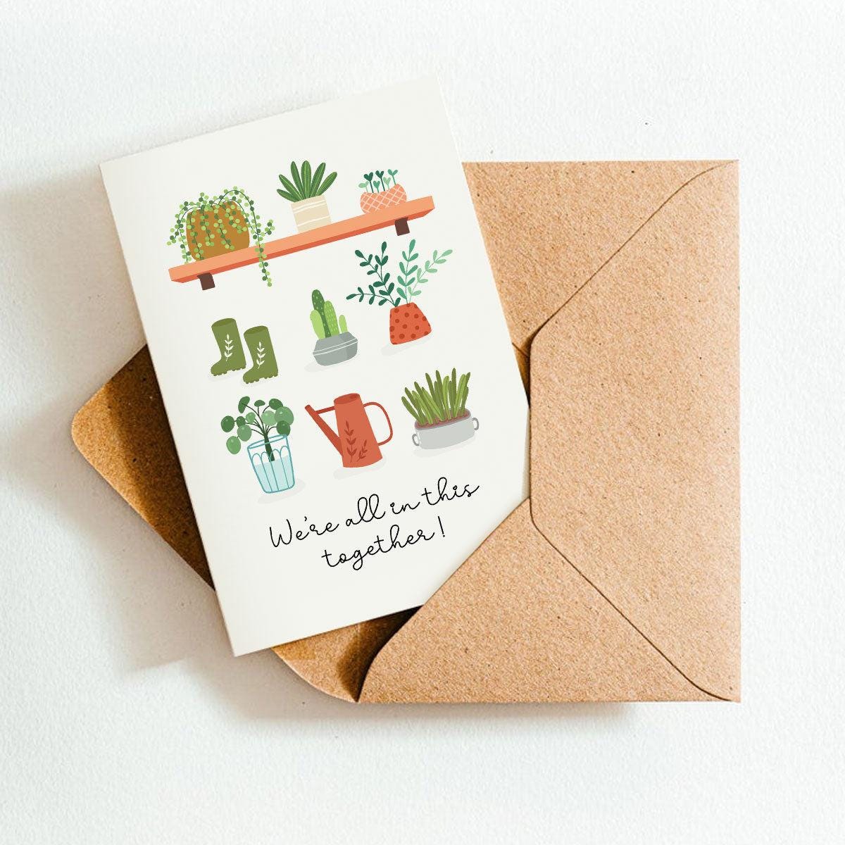 Greeting card with plant illustrations and 'We're all in this together!' text, placed on a brown envelope.
