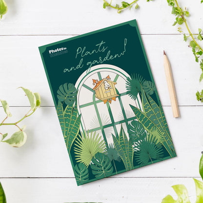 Notebook with a garden-themed cover on a white wooden surface with plants.