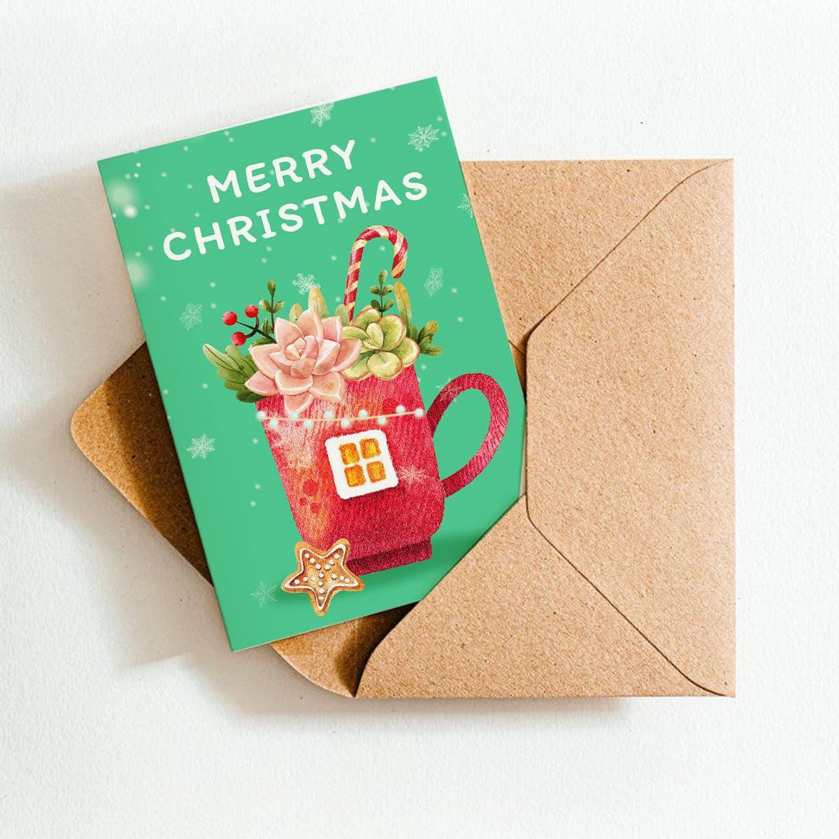 Christmas card with a red mug and succulents on a green background, placed inside a brown envelope.