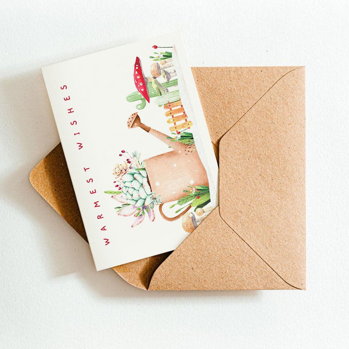 Greeting card with illustrations and 'Warmest Wishes' text, placed inside a brown envelope on a white background.