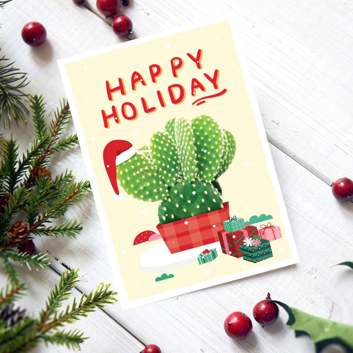 Christmas-themed card with cactus wearing a Santa hat and presents, surrounded by holiday decorations on a white surface.