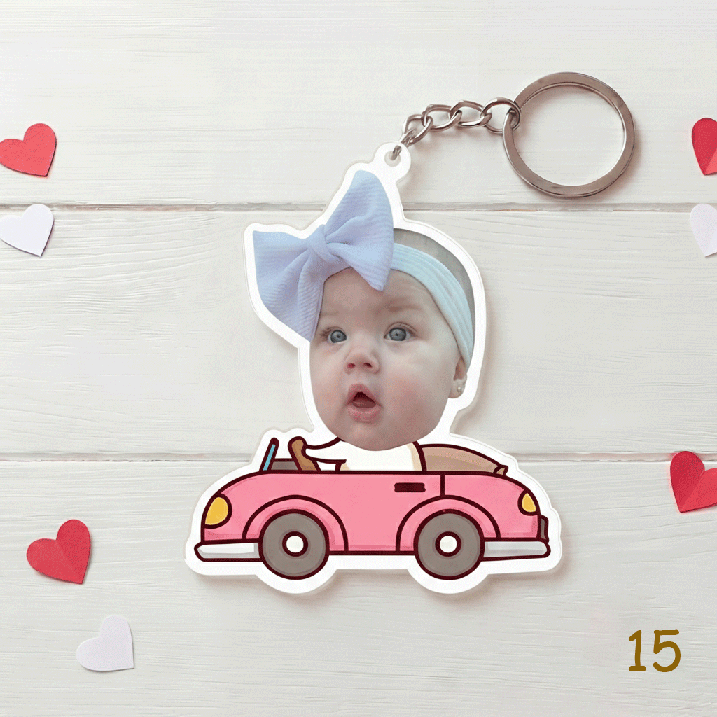 Keychain with a baby's face on a pink car design, surrounded by heart-shaped decorations on a light wooden background.