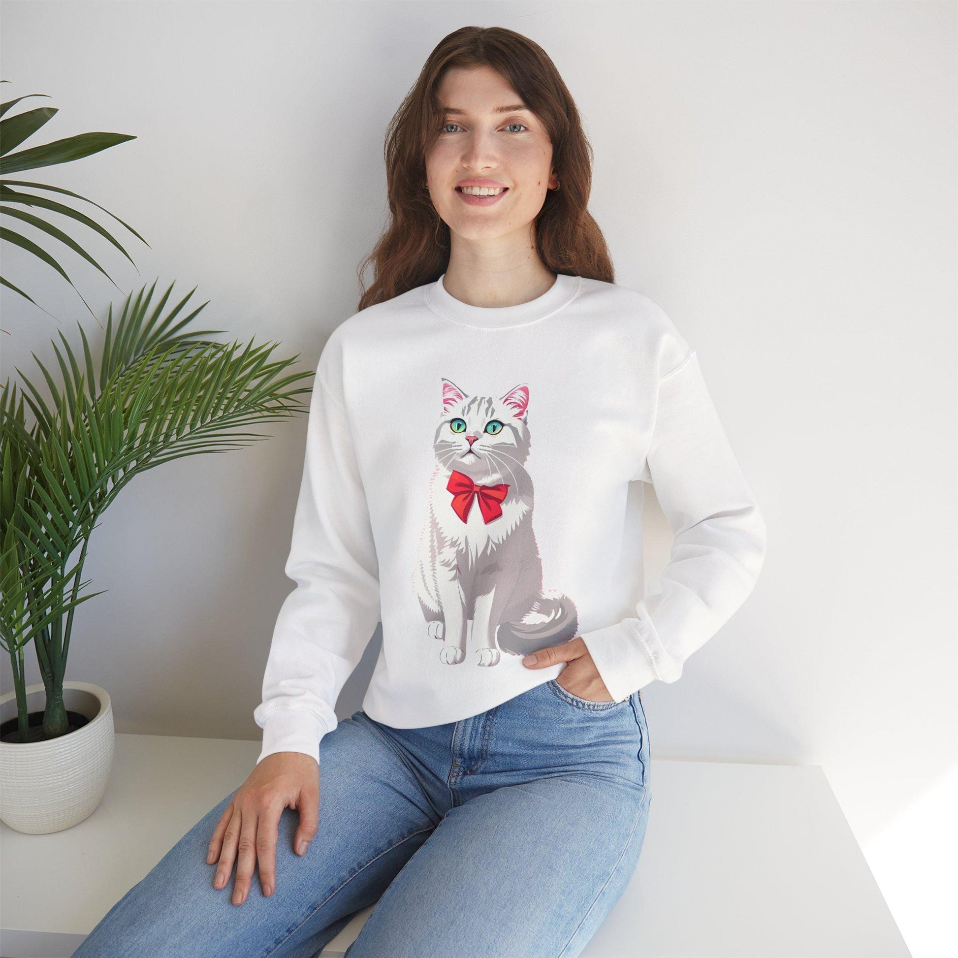 Woman wearing a white sweatshirt with a cat graphic, sitting on a white surface with a plant in the background.
