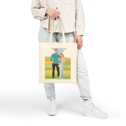 Person holding a tote bag with a printed design of two people standing in a field.
