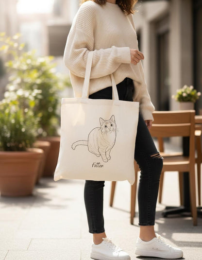 Person holding a tote bag with a cat illustration in an outdoor setting